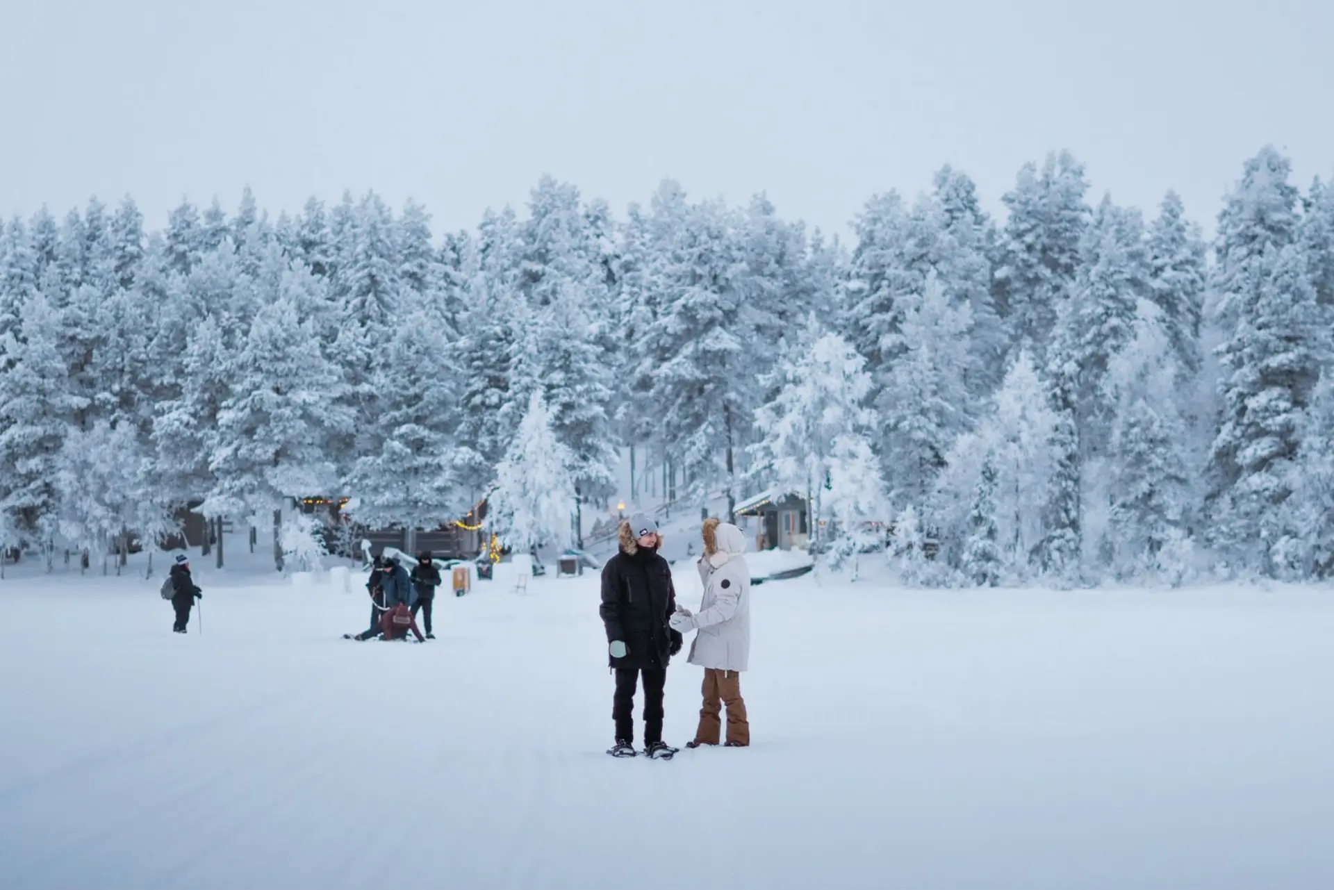 Visitors enjoying a cold winter day on a frozen lake surrounded by snowy forest in Levi, Finnish Lapland